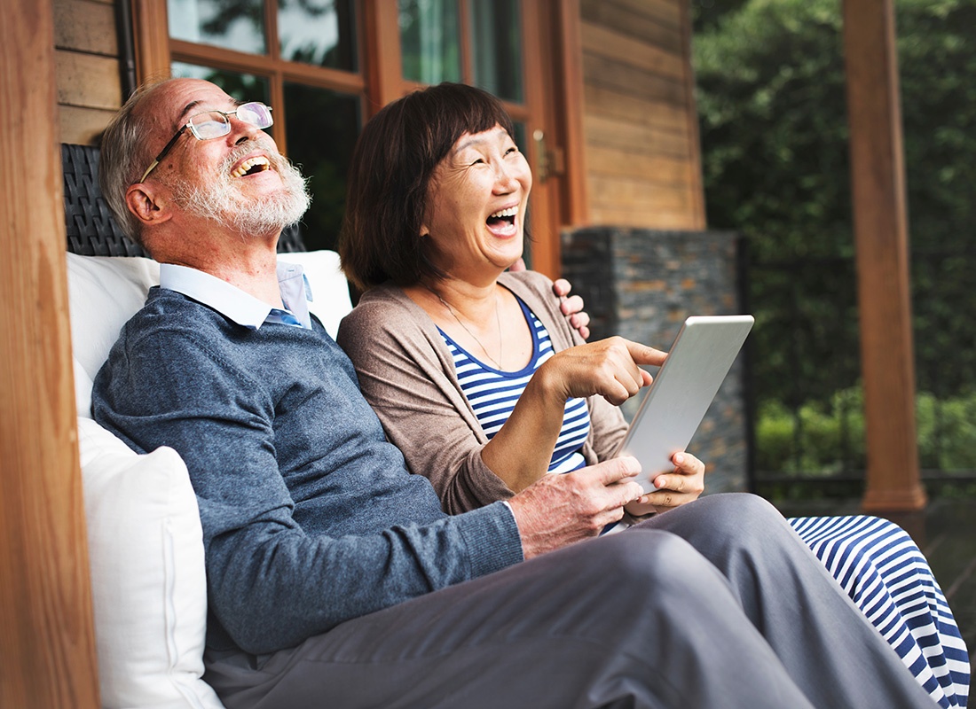 Read Our Reviews - Closeup Portrait of a Cheerful Elderly Couple Sitting on the Back Porch of Their Wooden Home Enjoying the Countryside Views While Holding a Tablet