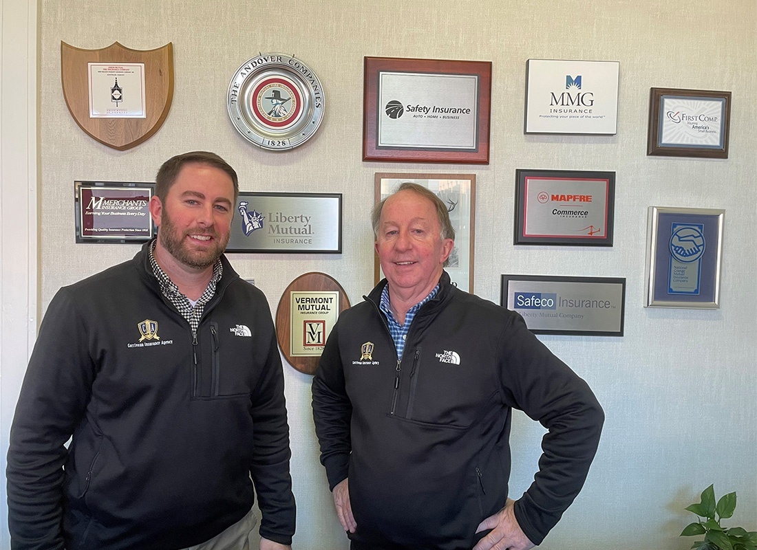 About Our Agency - Portrait of Phil and Ben from Corriveau Insurance Agency Standing in the Office in Front of a Wall with Awards and Partnerships